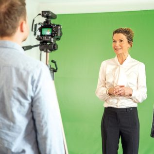 Eine der Trainierinnen bei einer Videoaufnahme für ein Lernprogramm. Sie steht vor einem Greenscreen.